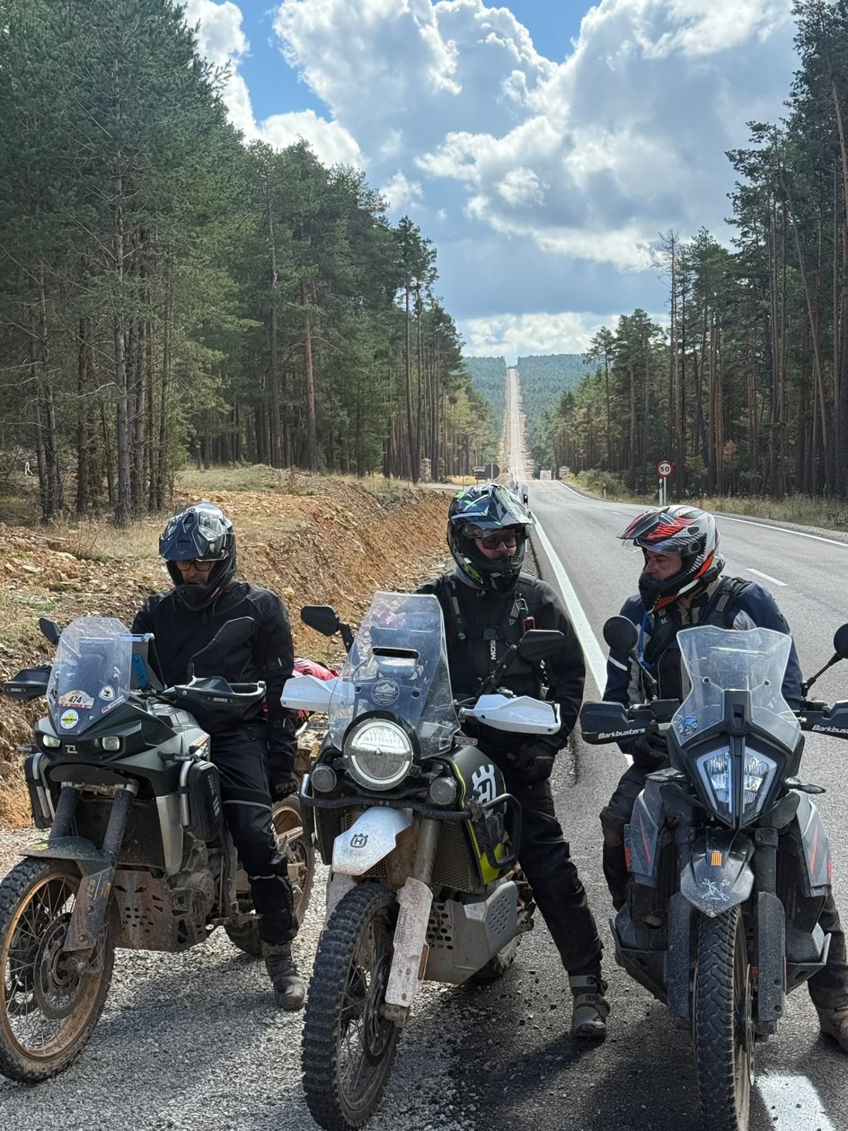 Tres pilotos con sus motos en una pista entre pinos