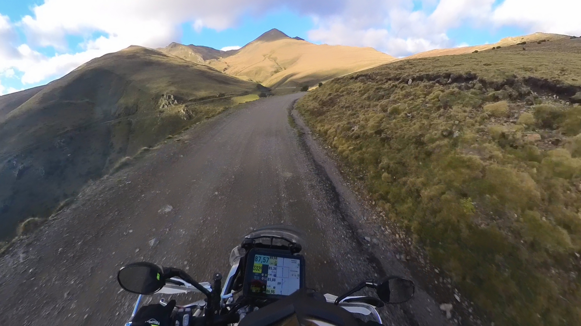 Tablet en el manillar de una moto trail mostrando un roadbook digital por una pista de alta montaña